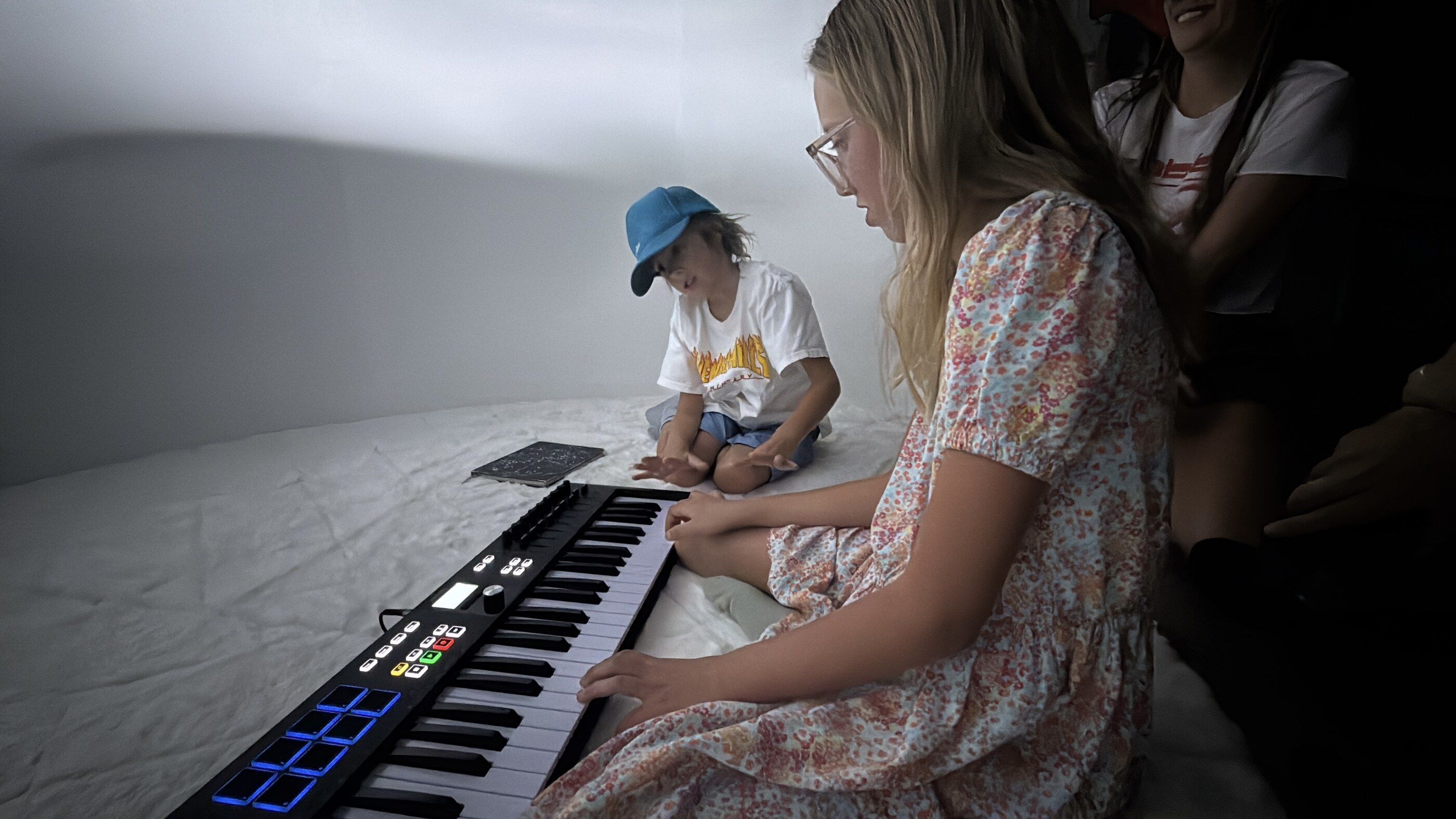 Two children at the keyboard inside the installation, the curved wall lit white behind them.